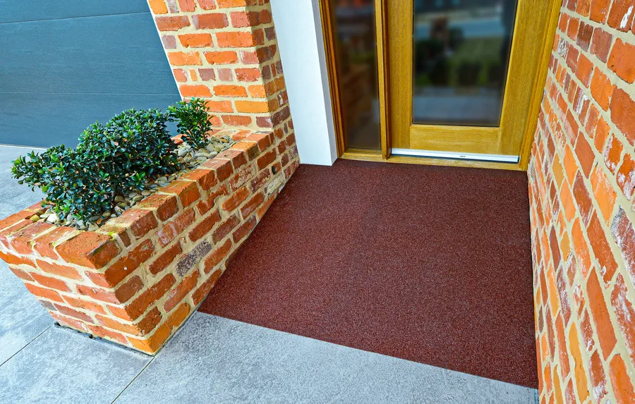 Brick red recycled rubber threshold surface at a timber front door between brick walls