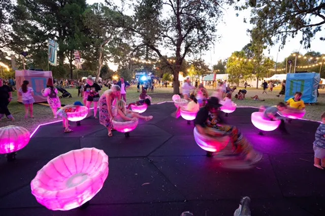 Festival goers at dusk on illuminated spinning seats set on dark rubber surfacing